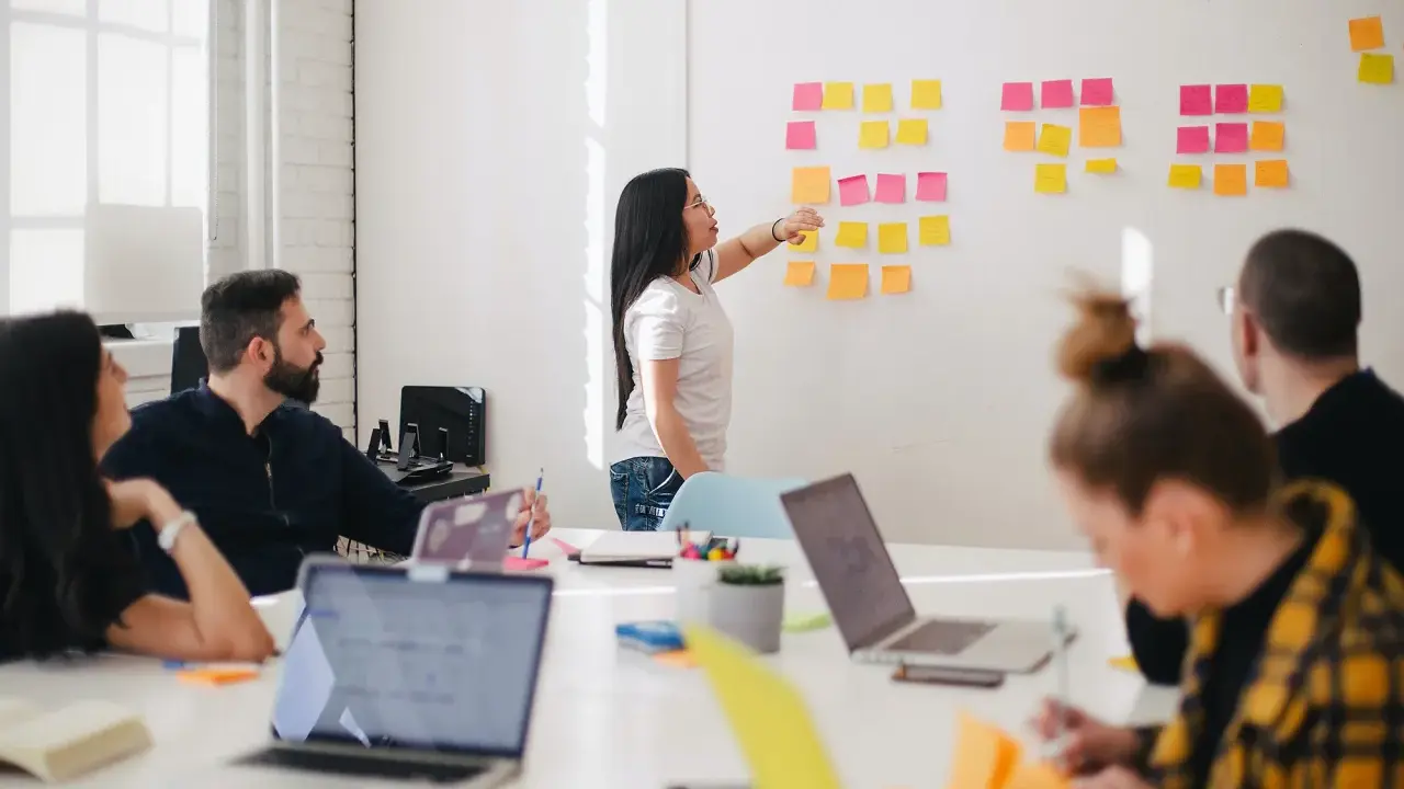 Une femme explique des techniques d'animation de réunion participative devant un mur couvert de post-its.