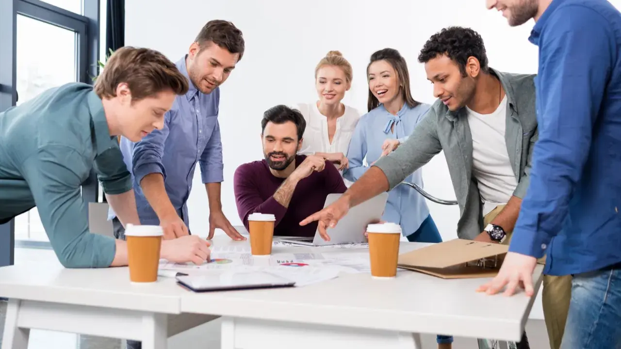Une équipe diversifiée participe à une réunion de projet animée, discutant des documents et d'un ordinateur portable autour d'une table.