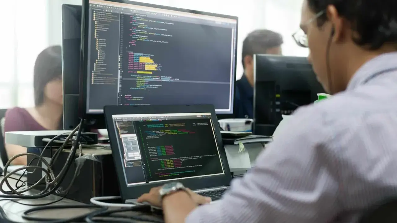 Un développeur Ruby on Rails concentré sur son code, devant plusieurs écrans affichant des lignes de programmation.