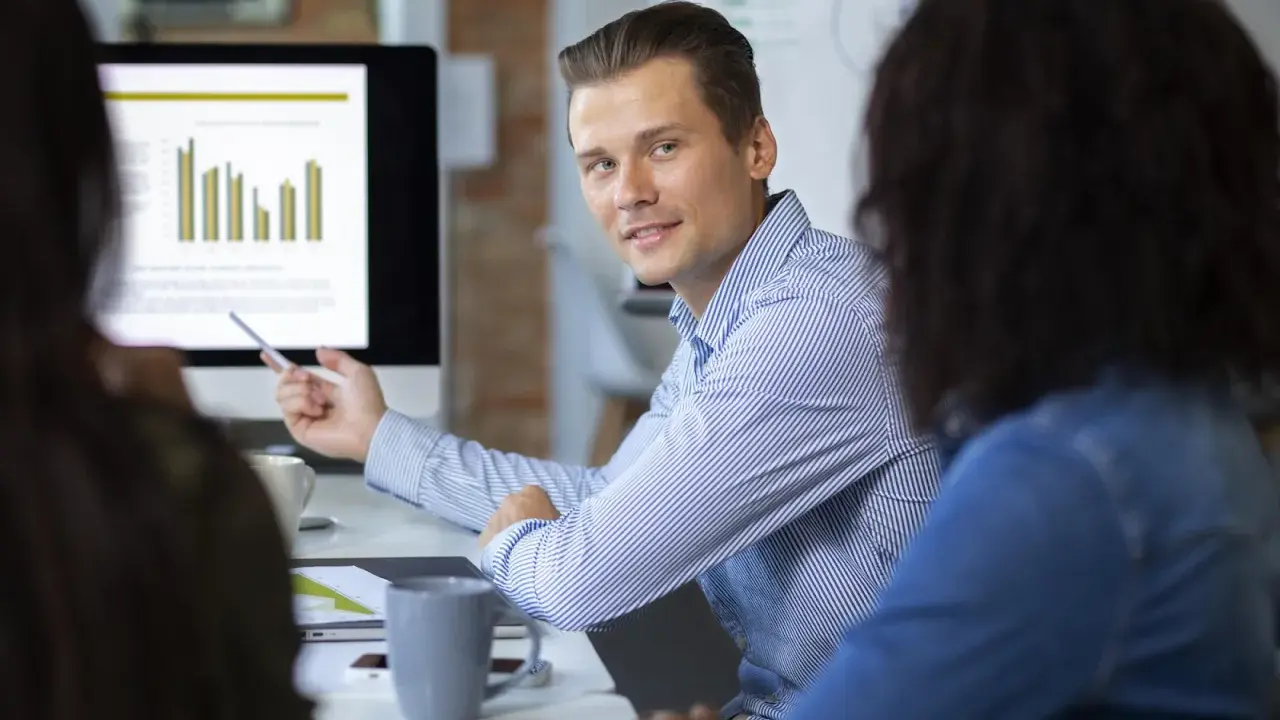 Un consultant en communication digitale explique des graphiques à ses collègues lors d'une réunion.