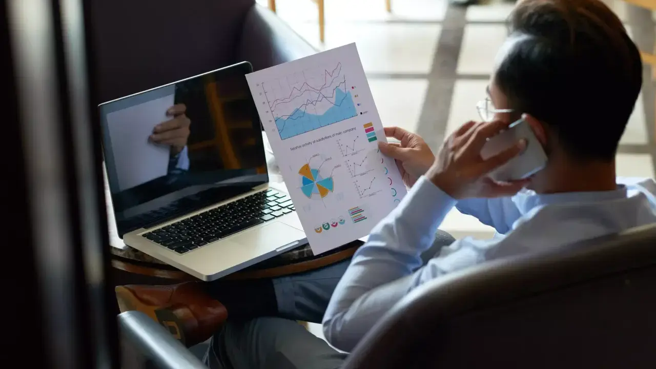 Homme d'affaires au téléphone, analysant des graphiques pour trouver des clients. Ordinateur portable ouvert à côté.