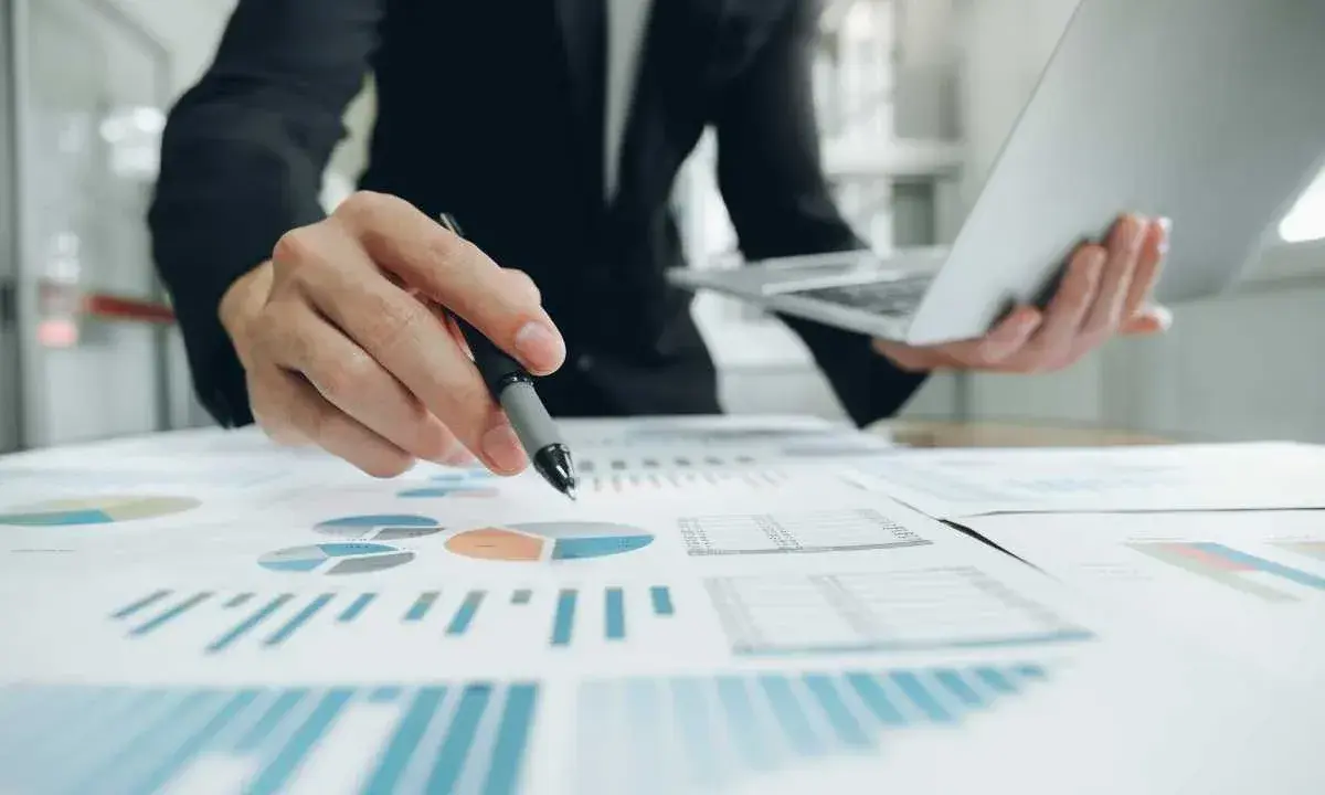 Un homme en costume analyse des graphiques et des diagrammes circulaires, tenant un stylo et un ordinateur portable. Il prépare un apport partiel d'actif.