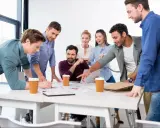 Une équipe diversifiée participe à une réunion de projet animée, discutant des documents et d'un ordinateur portable autour d'une table.