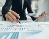 Un homme en costume analyse des graphiques et des diagrammes circulaires, tenant un stylo et un ordinateur portable. Il prépare un apport partiel d'actif.