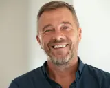 Un homme souriant, le chef de cabinet du PDG, avec une barbe poivre et sel et des yeux bleus pétillants.