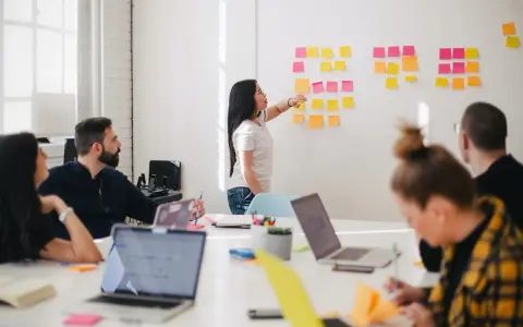 Une femme explique des techniques d'animation de réunion participative devant un mur couvert de post-its.