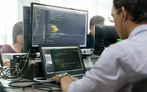 Un développeur Ruby on Rails concentré sur son code, devant plusieurs écrans affichant des lignes de programmation.