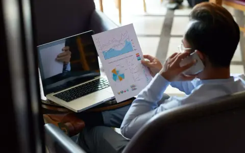 Homme d'affaires au téléphone, analysant des graphiques pour trouver des clients. Ordinateur portable ouvert à côté.