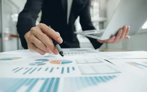 Un homme en costume analyse des graphiques et des diagrammes circulaires, tenant un stylo et un ordinateur portable. Il prépare un apport partiel d'actif.