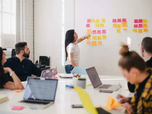 Une femme explique des techniques d'animation de réunion participative devant un mur couvert de post-its.