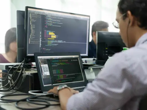 Un développeur Ruby on Rails concentré sur son code, devant plusieurs écrans affichant des lignes de programmation.