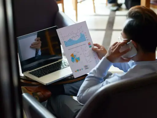 Homme d'affaires au téléphone, analysant des graphiques pour trouver des clients. Ordinateur portable ouvert à côté.