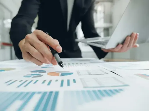 Un homme en costume analyse des graphiques et des diagrammes circulaires, tenant un stylo et un ordinateur portable. Il prépare un apport partiel d'actif.