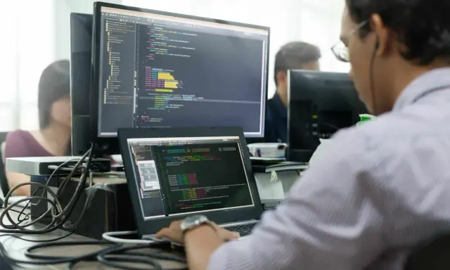 Un développeur Ruby on Rails concentré sur son code, devant plusieurs écrans affichant des lignes de programmation.