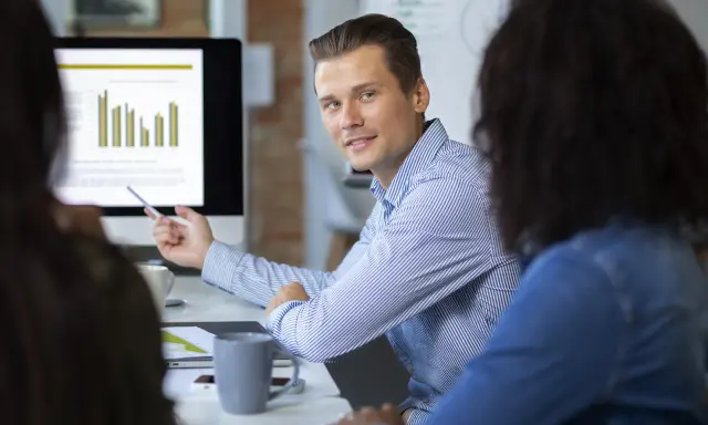 Un consultant en communication digitale explique des graphiques à ses collègues lors d'une réunion.