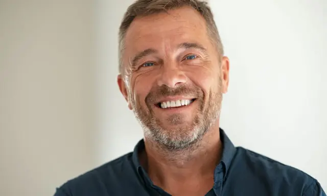 Un homme souriant, le chef de cabinet du PDG, avec une barbe poivre et sel et des yeux bleus pétillants.