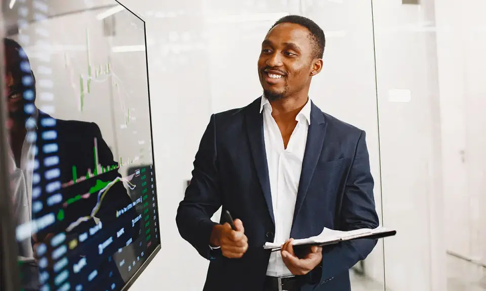 Un key account executive souriant présente des graphiques financiers sur un écran.