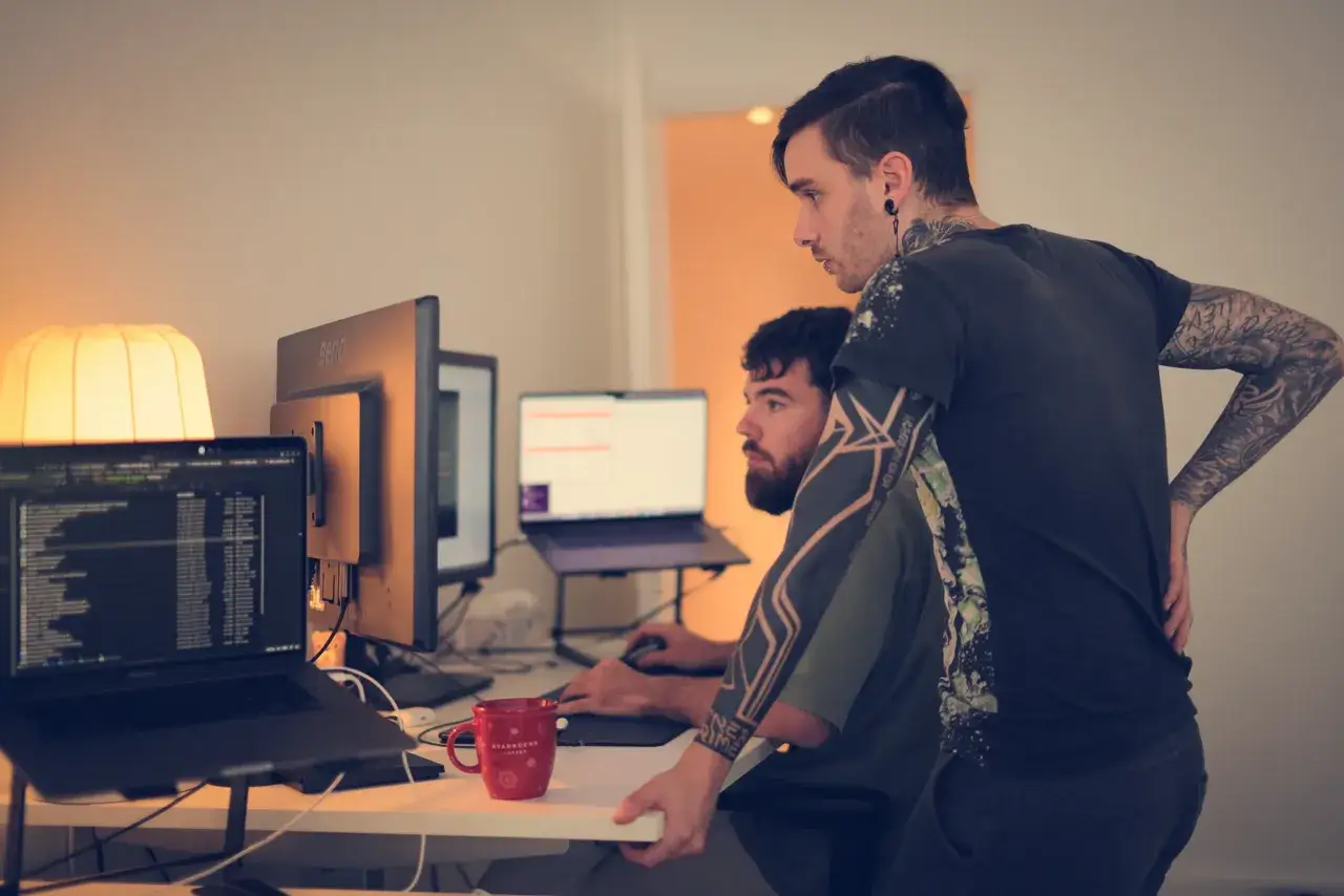 Deux développeurs Ruby on Rails collaborent sur un projet, l'un regardant l'écran, l'autre expliquant une ligne de code.