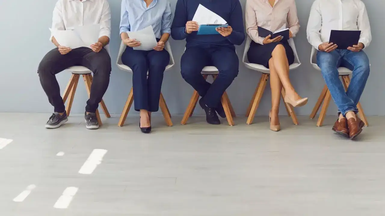 Cinq personnes assises, attendant un entretien. Leurs CV en main, ils espèrent négocier un bon salaire, peut-être pour un poste de chasseur de tête.