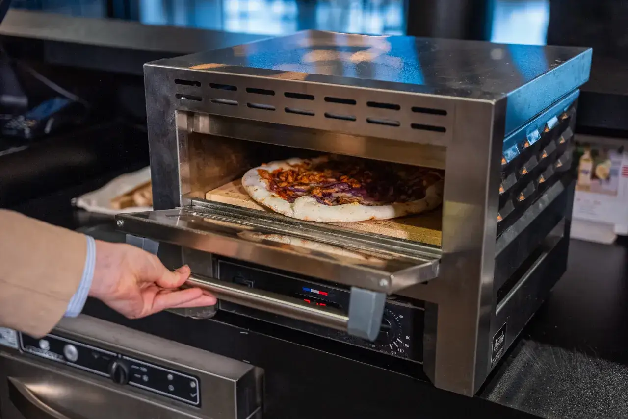 Main d'un homme ouvrant un four &agrave; pizza o&ugrave; cuit une pizza. Le d&eacute;but d'une belle aventure pour ouvrir une pizzeria.